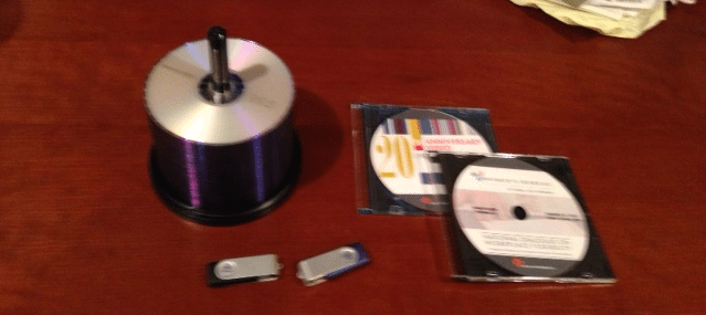 Photo of a stack of DVDs with two custom DVDs in cases and two thumb drives
