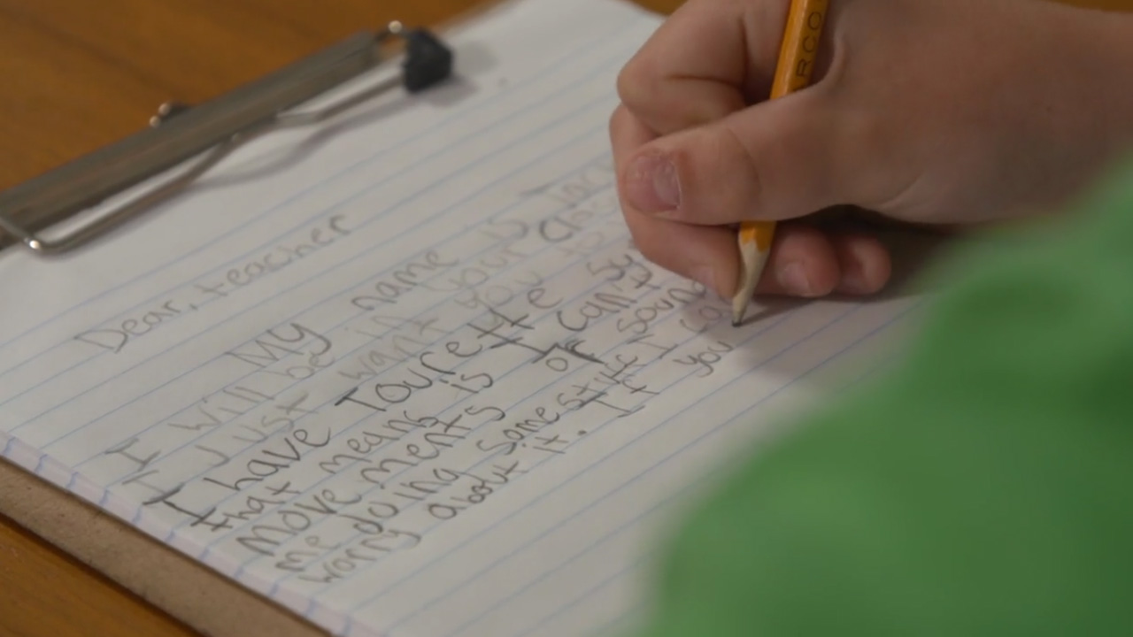 close up of elementary student writing on pad of paper to teacher used in short scripted video intro Portfolio %page