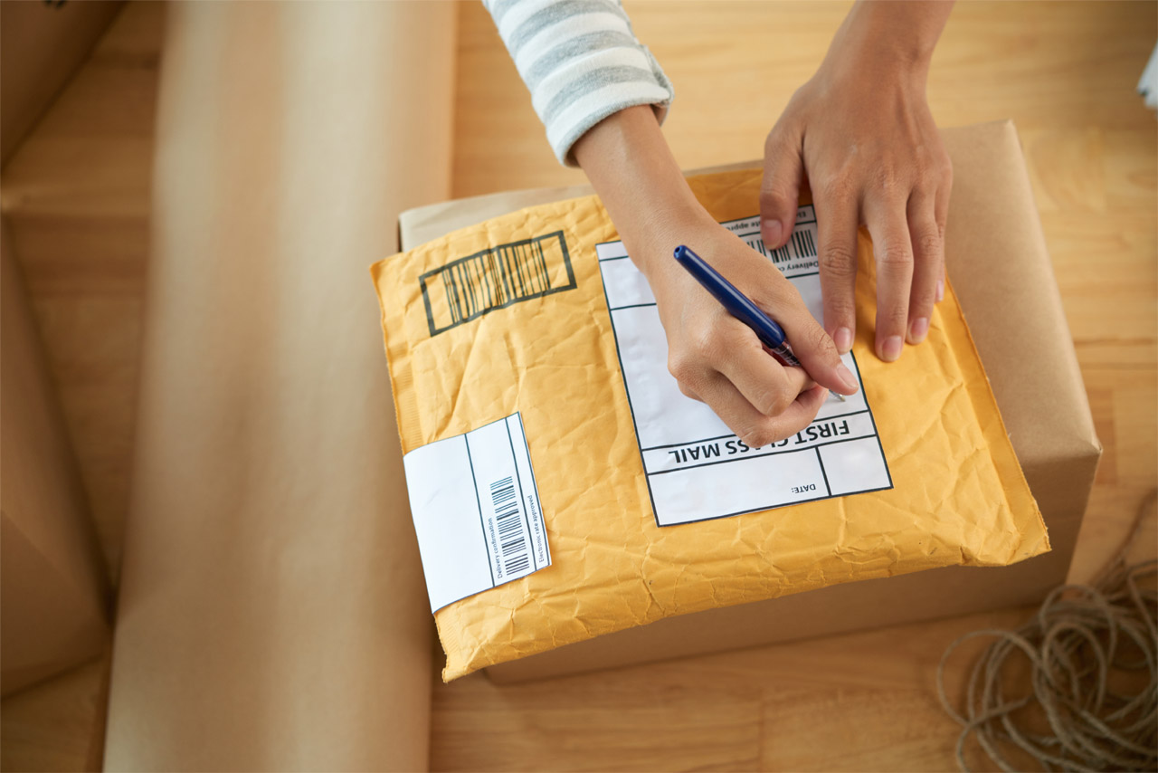 woman-home-office-addressing-small-package-mailing woman addressing small package for mailing from home office