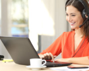 Image of woman wearing orange blouse on conference call in home office on laptop and with cup of coffee